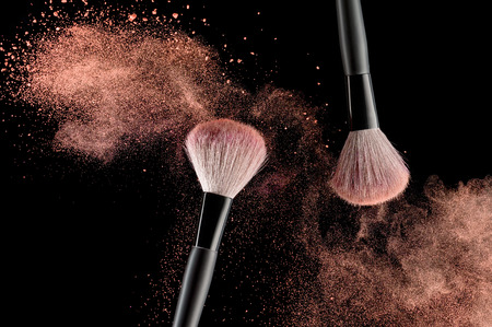 Make-up brush with pink powder explosion on black background Make-up brush with pink powder explosion on black background