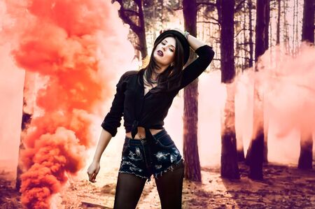 Beautiful woman with orange smoke behind her in the forest.の写真素材