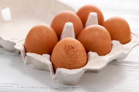 Six yellow eggs in a cardboard tray on a white wooden table.の写真素材