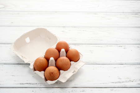 Six yellow eggs in a cardboard tray on a white wooden table.の写真素材