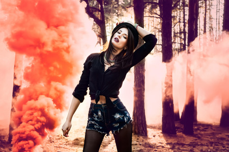 Beautiful woman with orange smoke behind her in the forest.の写真素材