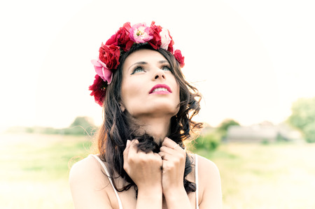 Attractive young woman with floral wreath on her head with sunset in background. Shallow DOF. Vintage stylized.の写真素材