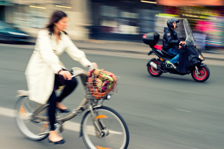 Woman riding a bicycle in the city, motorcyclist on background, motion blur.の写真素材