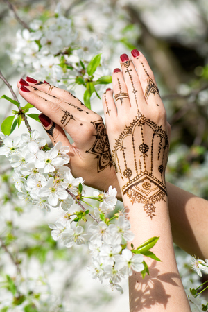 Red manicured hands with Mehndi in spring cherry blossom, Indian tradition. Vertical composition.の写真素材