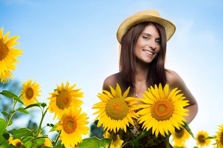 Young woman imitating her breast with two sunflowers in a fieldの写真素材