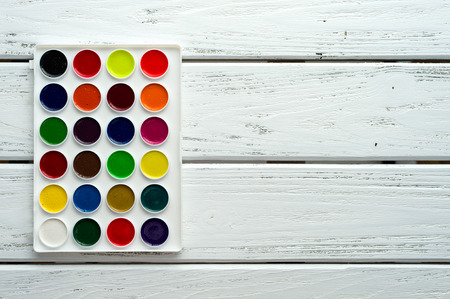 Desk of creative worker. Paints on wooden white background, top view, with copy space.の写真素材