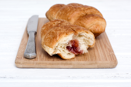 Croissant and a table knife on the wooden chopping board. Close-up, shallow DOF. Horizontal composition.の写真素材