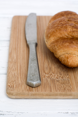 Croissant and a table knife on the wooden chopping board. Close-up, shallow DOF. Vertical composition.の写真素材