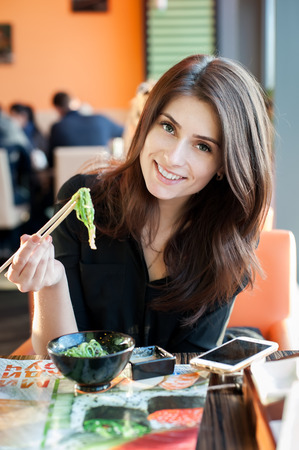 Young smiling woman eating japanese seaweed salad (Chuka) in a sushi restaurant.の写真素材