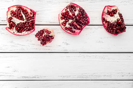 Pieces of ripe juicy pomegranate and pomegranate seeds on a white wooden plank background.の写真素材