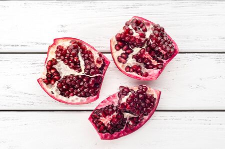 Pieces of ripe juicy pomegranate and pomegranate seeds on a white wooden plank background.の写真素材