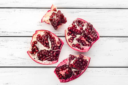 Pieces of ripe juicy pomegranate and pomegranate seeds on a white wooden plank background.の写真素材