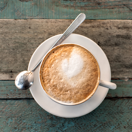Cappuccino cup with spoon  on old rustic wooden table background. Photo taken outdoors in tuscan cafe. Top view. Square composition.の写真素材