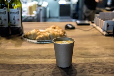 Take away paper cup with tasty hot cappuccino on wooden counter, close-up, selective focus, shallow DOF. Interior shot.の写真素材