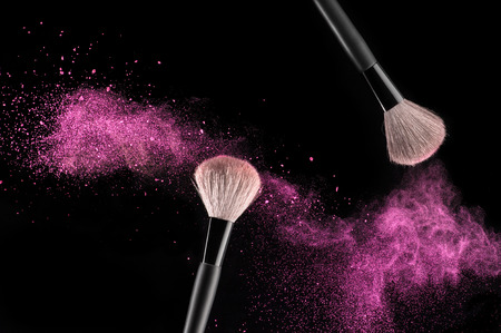 Make-up brushes with pink powder explosion on black backgroundの写真素材
