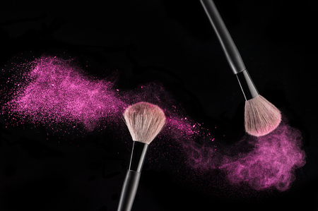 Make-up brushes with pink powder explosion on black backgroundの写真素材