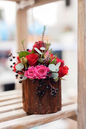 Flower arrangement of multi-colored roses and berries in wooden stump, floristic art close-up.の写真素材