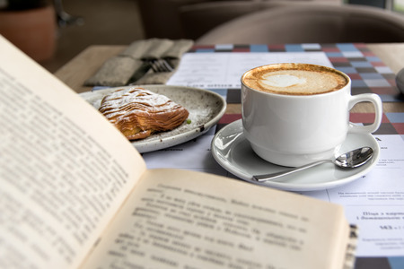 Still life details, cup of Cappuccino and cake with book on table in coffee shop cafe, shallow DOF.の写真素材