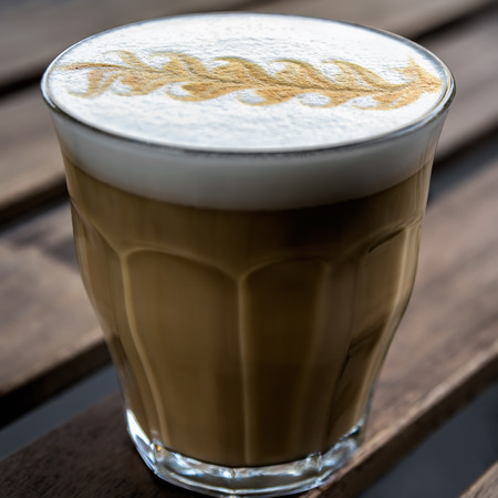 ?appuccino coffee with  leaf shape foam top in a glass on wooden planks background, shallow DOF, soft focus. Square composition.の写真素材