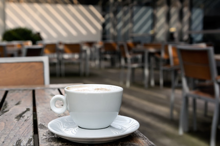 White cup with hot cappuccino on wooden table on summer terrace cafe.の写真素材