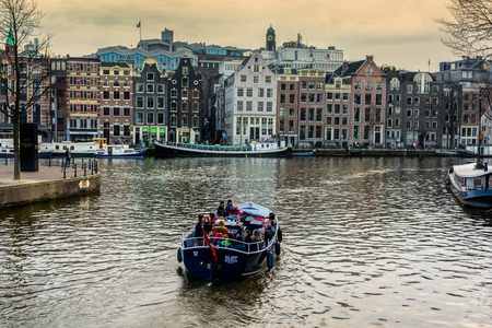AMSTERDAM, NETHERLANDS - APRIL 10, 2018: Amsterdam canal with tourist boat and typical dutch houses on the background in the evening.のeditorial素材