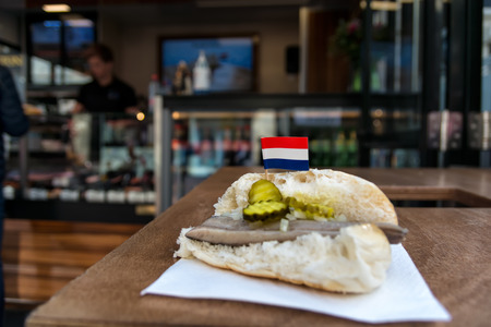 Traditional dutch snack, seafood sandwich with herring, onions and pickled cucumber. Broodje haring on the wooden table. With flag of Netherlands.の写真素材
