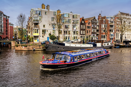AMSTERDAM, NETHERLANDS - APRIL 10, 2018: Amsterdam canal with typical dutch houses and touristic boat on foreground, Amsterdam, Netherlands.の写真素材