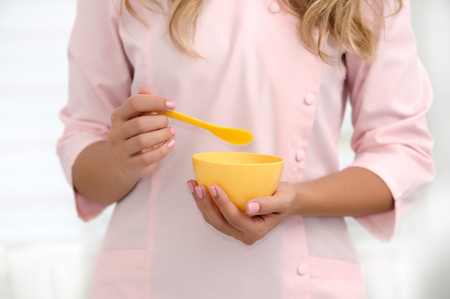 The hands of a beautician stir the ingredients in a yellow cup for applying the mask on the skin. Cosmetology concept. Horizontal composition. Shallow dof, soft focus.の写真素材