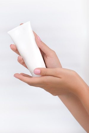 Hand skin care. Female hands holding cream tube, beautiful beautician woman hands with close-up over natural white background. Nails Beauty And Body Care Concept. Shallow DOF.の写真素材