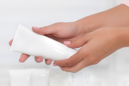 Hand skin care. Female hands holding cream tube, beautiful beautician woman hands with close-up over natural white background. Nails Beauty And Body Care Concept. Shallow DOF.の写真素材