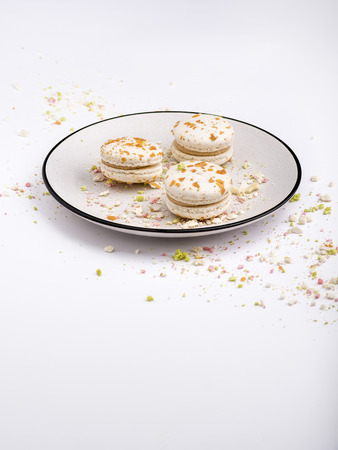 Three beige white macaroon cookies with multicolored crumb on white plate with blue border. Food background, shallow DOF, soft focus, copy space.の写真素材