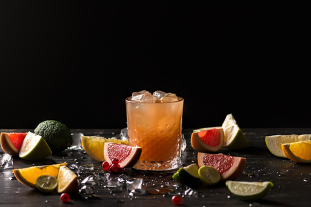 Glass of orange juice and ice with fruits slices (orange, grapefruit, lime and red currant) over black background. Close-up, shallow DOF, soft focus, with copy space.の写真素材