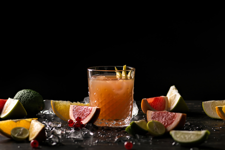 Glass of orange juice and ice with fruits slices (orange, grapefruit, lime and red currant) over black background. Close-up, shallow DOF, soft focus, with copy space.の写真素材