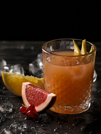 Glass of orange juice and ice with fruits slices (orange, grapefruit, lime and red currant) over black background. Close-up, shallow DOF, soft focus, with copy space.の写真素材