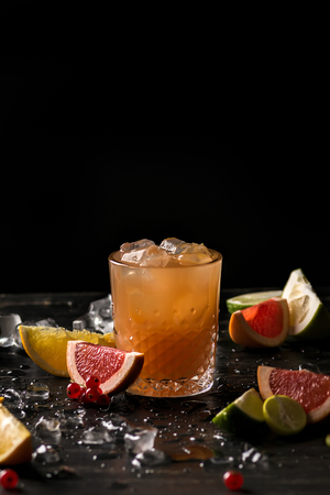 Glass of orange juice and ice with fruits slices (orange, grapefruit, lime and red currant) over black background. Close-up, shallow DOF, soft focus, with copy space.の写真素材