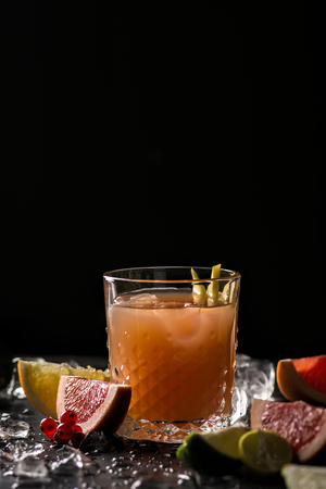 Glass of orange juice and ice with fruits slices (orange, grapefruit, lime and red currant) over black background. Close-up, shallow DOF, soft focus, with copy space.の写真素材
