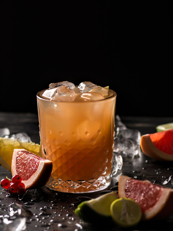 Glass of orange juice and ice with fruits slices (orange, grapefruit, lime and red currant) over black background. Close-up, shallow DOF, soft focus, with copy space.の写真素材