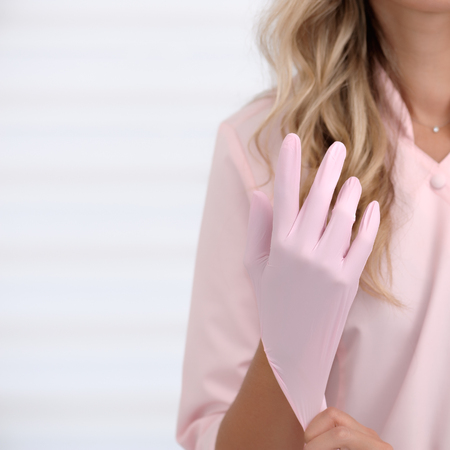 Beautician woman putting on pink rubber gloves against body background. Body and health care female health concept. Shallow dof, soft focus. Square composition.の写真素材