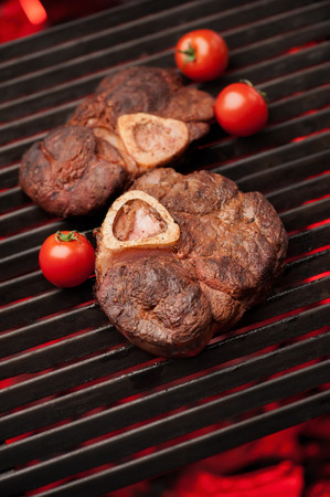Two grilling steaks with cocktail tomatoes on the flaming grill, close-up, selective focus. Photo taken on workshop.の写真素材