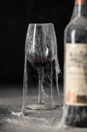Grunge wine glass with red wine and bottle of wine in a cobweb in the dark cellar. Photo taken on workshop.の写真素材
