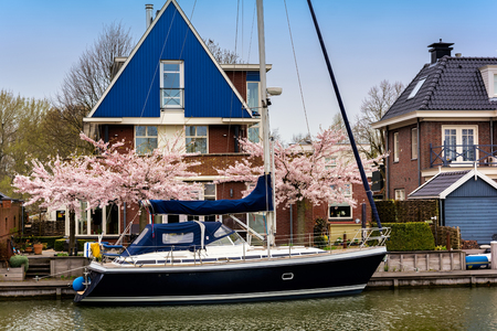 EDAM, NETHERLANDS - APRIL 14, 2018: Traditional dutch house with yacht and blooming spring tree on the canal waterfront. Edam is a small village in the district Nordholland, Netherlands.のeditorial素材