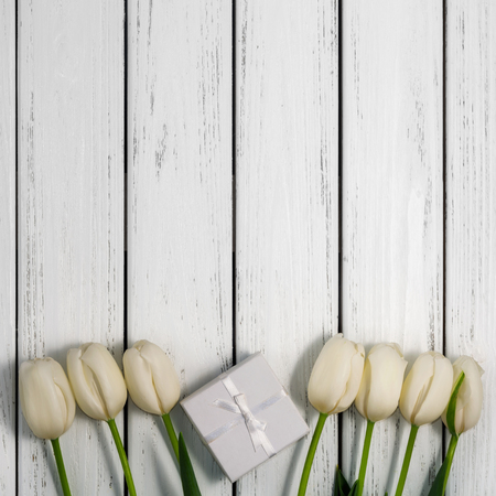 Beautiful white tulips with gift box on white wooden background. Top view, copy space. Space for text. Square postcard template.の写真素材