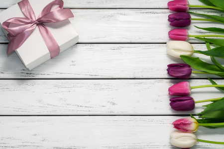 Beautiful multicolored tulips with gift on white wooden background. Top view, copy space. Space for text. Horizontal postcard template. Spring flowers concept. Happy Mother's, Valentine's day.の写真素材