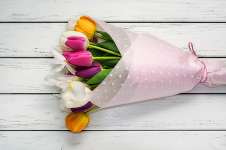 Bouquet of multicolored tulips in paper wrapper on white wooden table.の写真素材