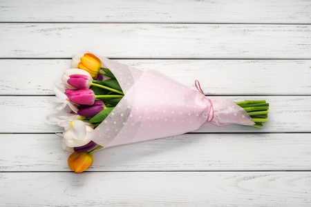 Bouquet of multicolored tulips in paper wrapper on white wooden table.の写真素材