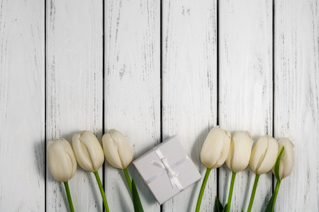 Beautiful white tulips with gift box on white wooden background. Top view, copy space. Space for text. Postcard template. Horizontal shot.の写真素材