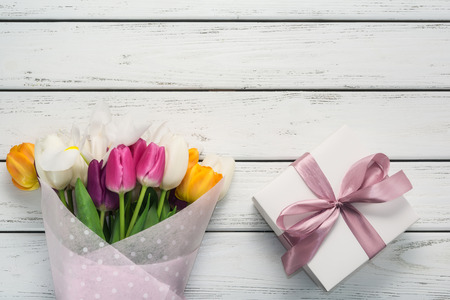 Bouquet of multicolored tulips in paper wrapper with gift box on white wooden table. Copy space.の写真素材