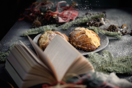 Christmas concept - book, christmas decorations and croissants on table with snow. Christmas postcard. Selective focus, shallow DOF. Photo taken on the workshop. Photo taken on the workshop.の写真素材