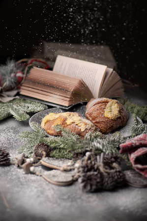Christmas concept - book, christmas decorations and croissants on table with snow. Christmas postcard. Selective focus, shallow DOF. Photo taken on the workshop. Photo taken on the workshop.の写真素材