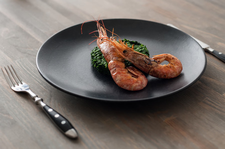 Two shrimps on spinach in black plate. Angle view, studio shot. Photo taken on the workshop.の写真素材